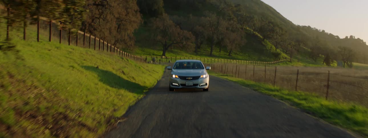 Grey car drives on a country road between farmlands at sunset in the countryside