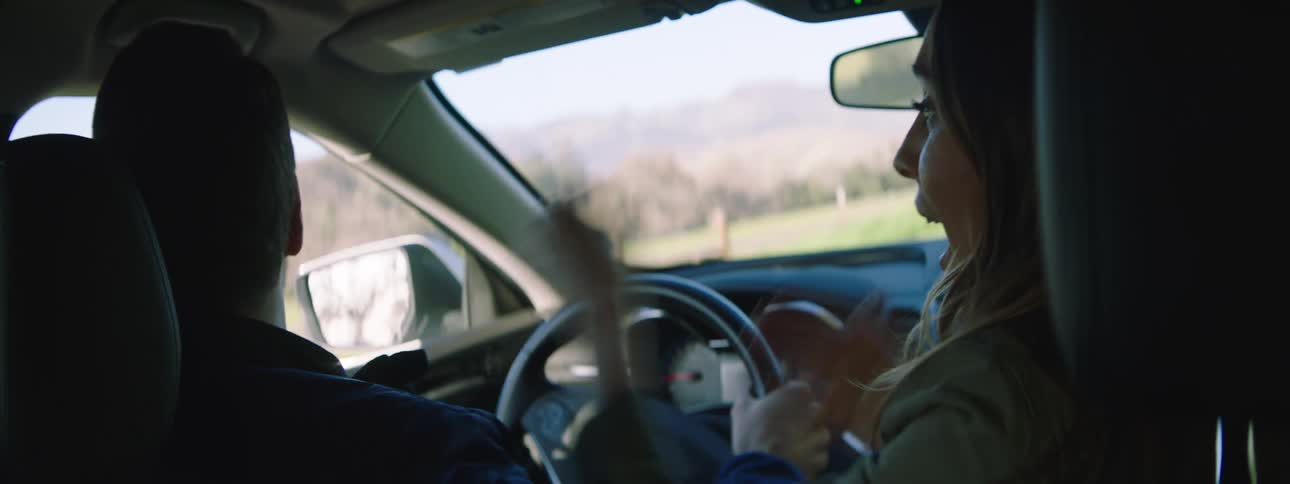 Man and woman travel in a vehicle as the point to something outside the vehicle and laugh