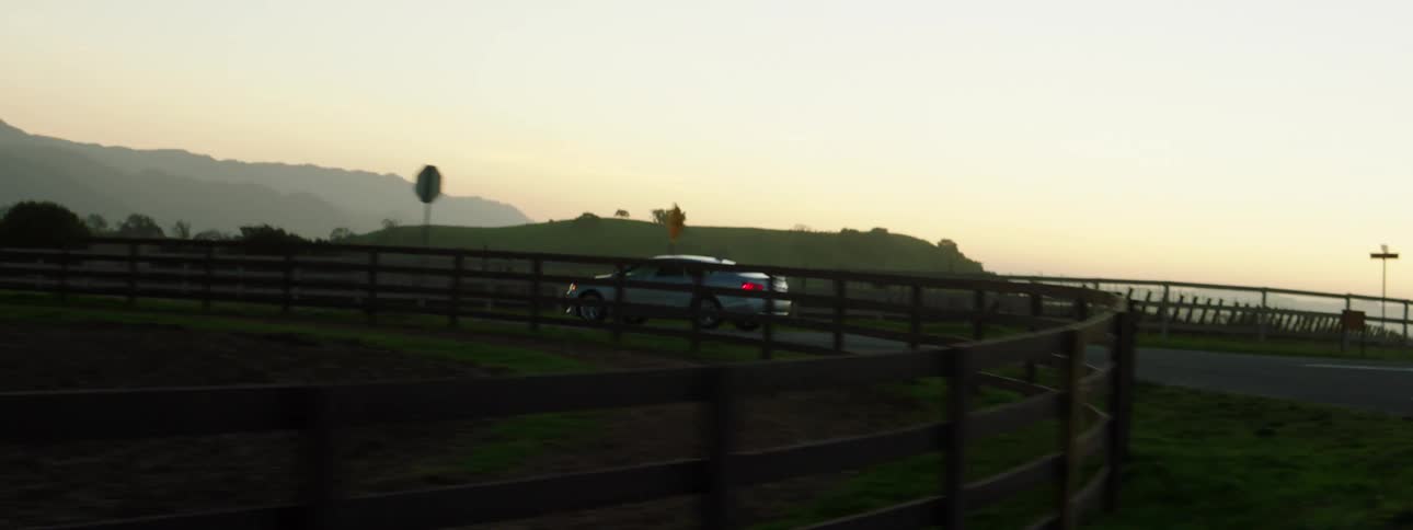 A car is driving in a rural area at dusk