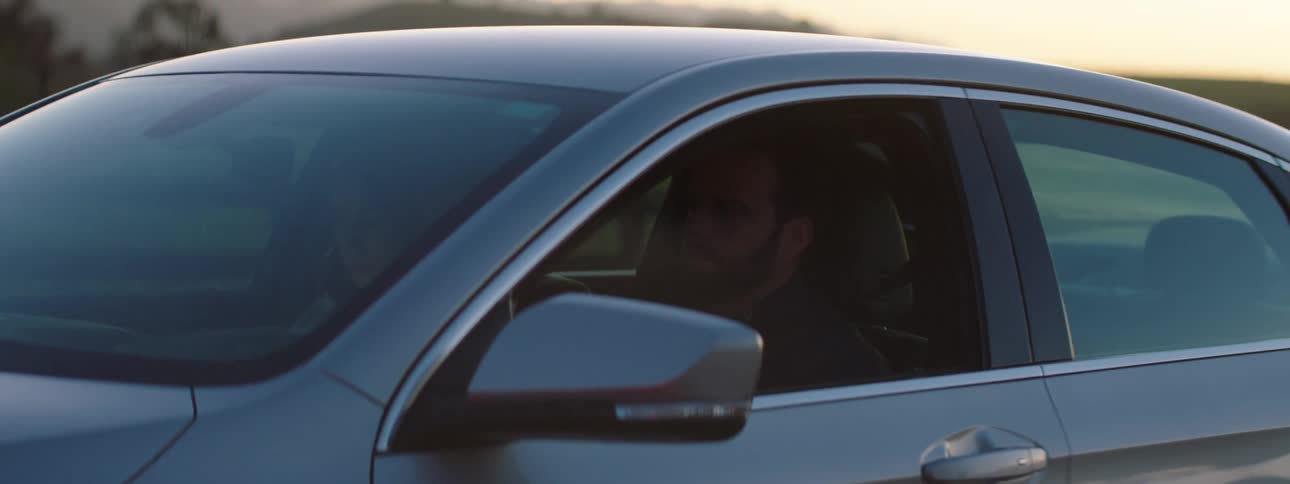 Couple driving a car on a rural road at sunset