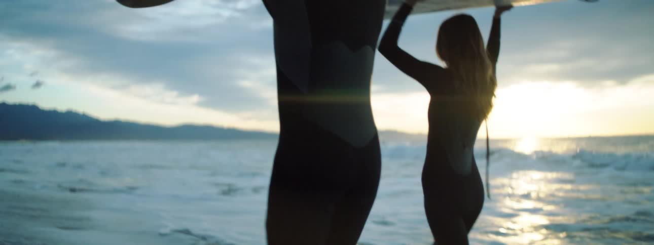 Two surfers carry their boards on the beach