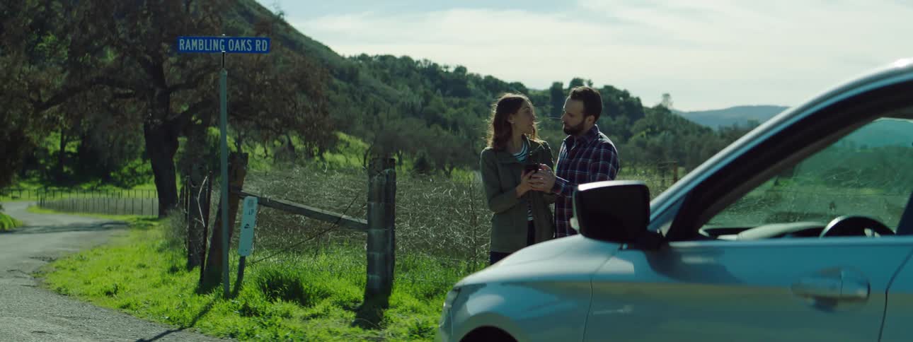 A man and woman stopped by the side of a road in front of a field look at a cell phone