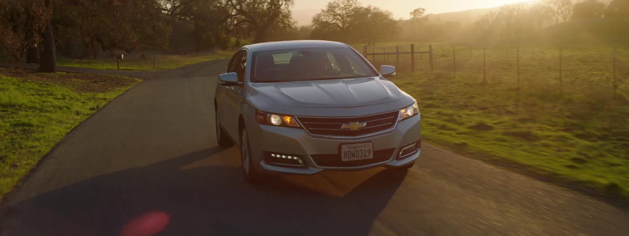 Grey car drives on a country road by a farmland at sunset