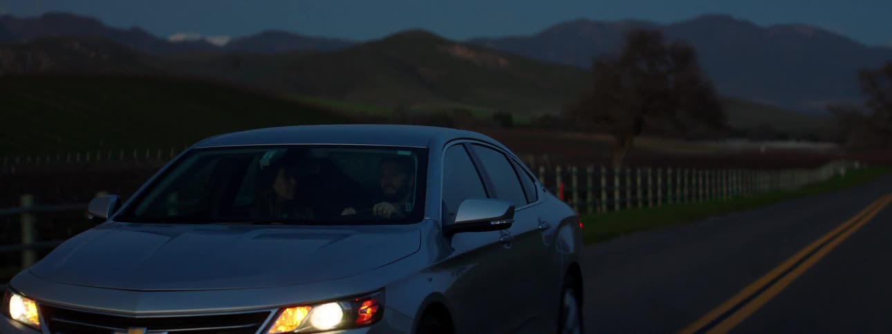 A car with headlights on driving on a rural road in the early morning