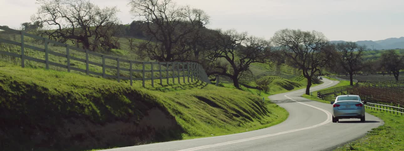 A car travels along a winding road through the countryside on a sunny day