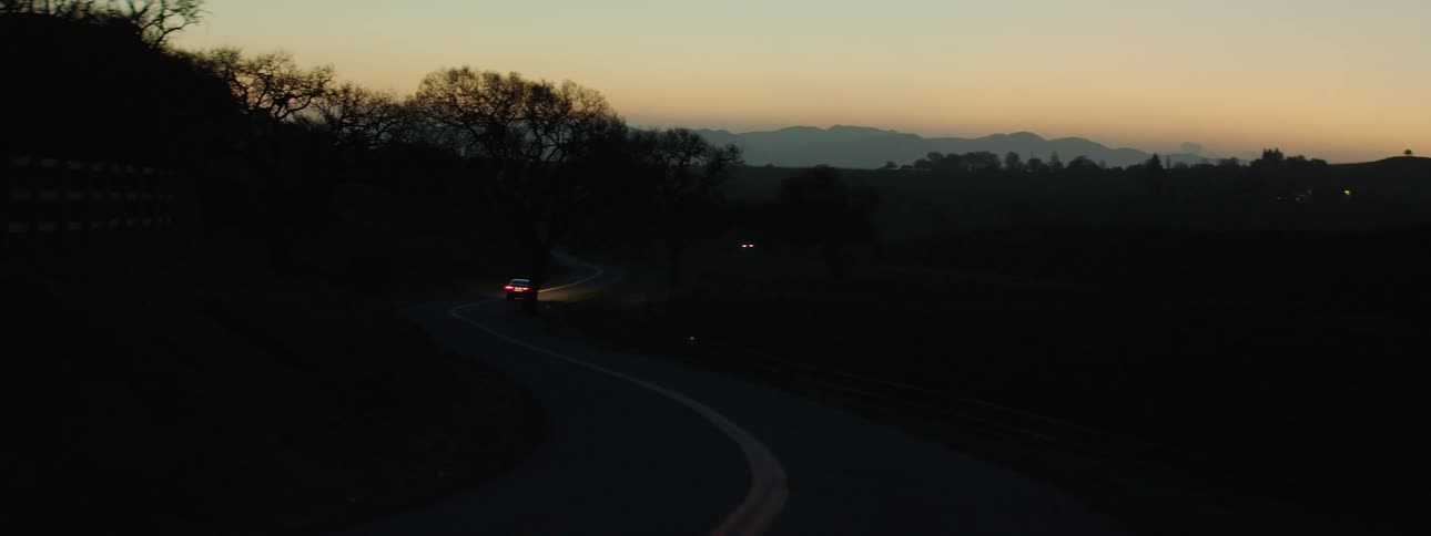 A car is driving down a road at dusk