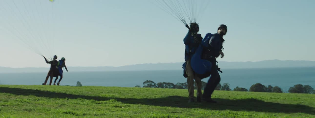 Two pairs of people on a hill prepare to paraglide