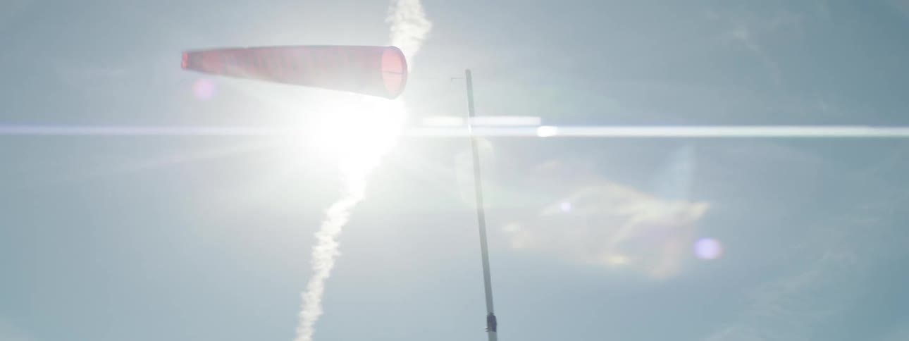 A wind sock is blown by a strong breeze of wind beneath a very sunny sky