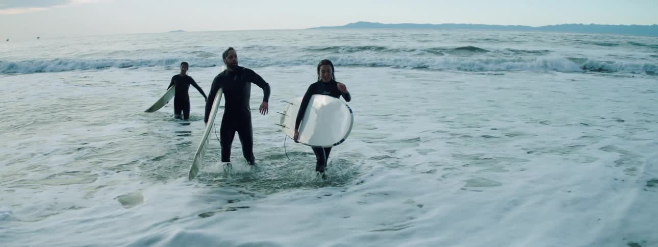 Three people walk out of the ocean carrying surf boards