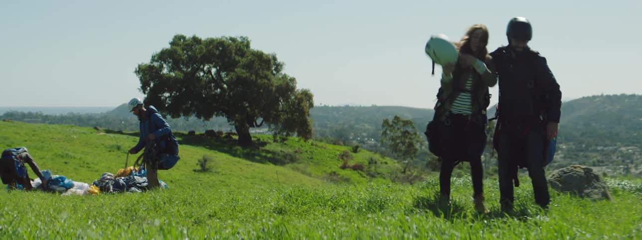A man and woman in paragliding equipment high five while walking out of frame