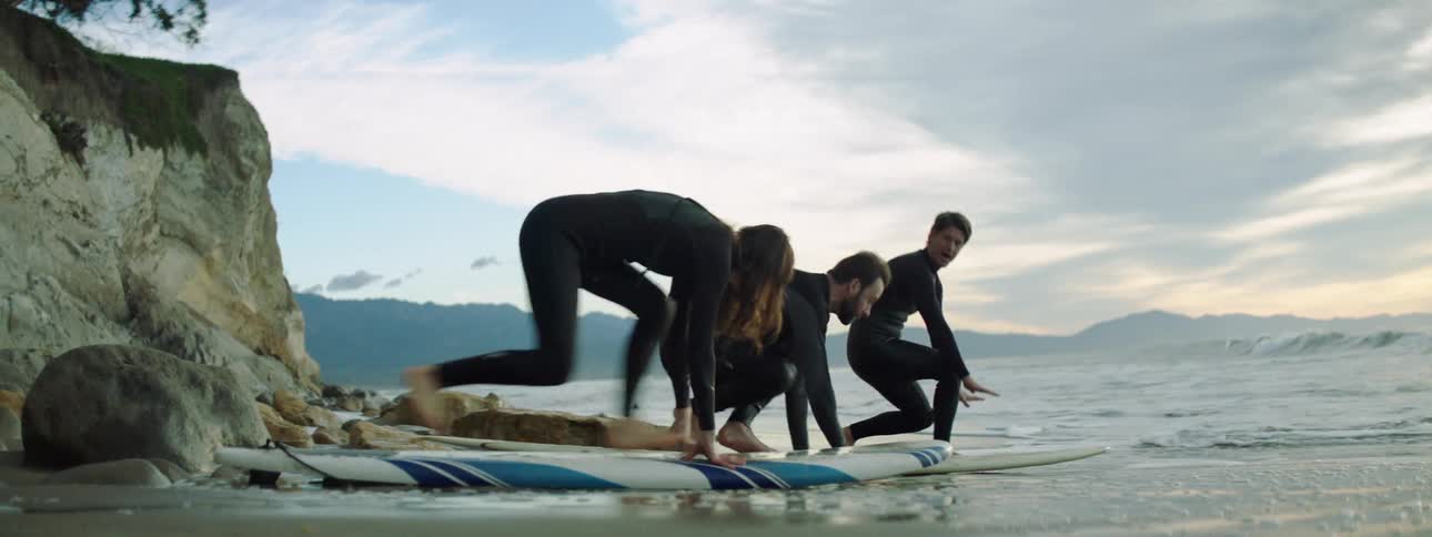An instructor teaches two aspiring surfers how to surf by leading them in drills on the beach