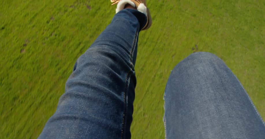 A person in jeans and boots kicks their legs while parachuting