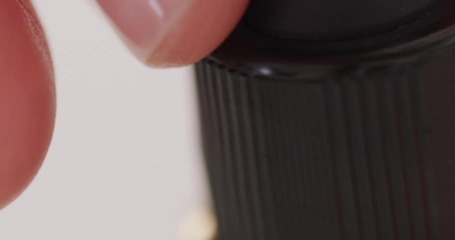 Close up of a hand unscrewing a dropper cap filled with yellow clear liquid