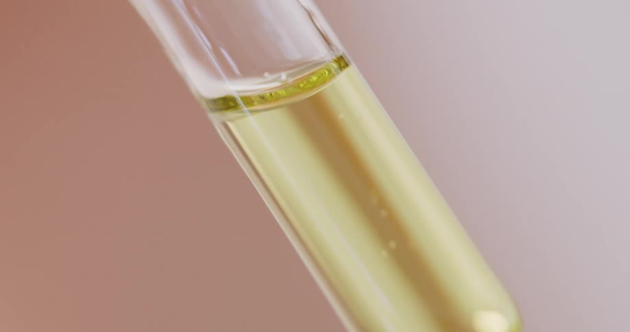 A thin transparent tube is filled with a viscous amber liquid that is slowing dripping out of the bottom