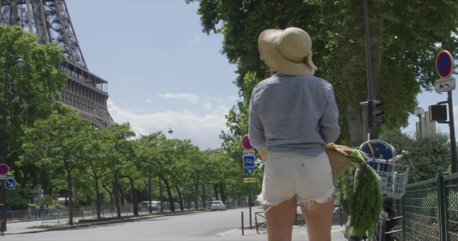 A woman carrying a basket of produce as she walks along a street next to the eiffel tower