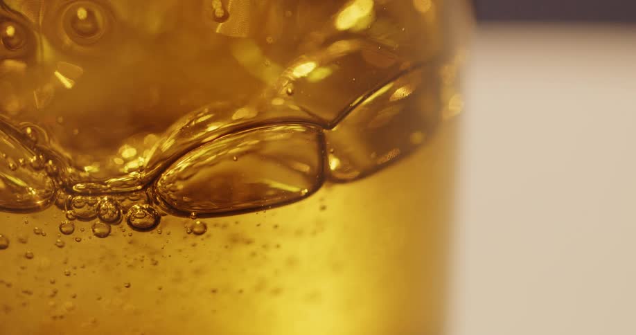 Shadow passes over amber colored liquid with bubbles in glass