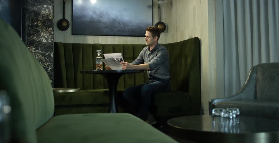 A man sitting next to a table drinking a glass of alcohol
