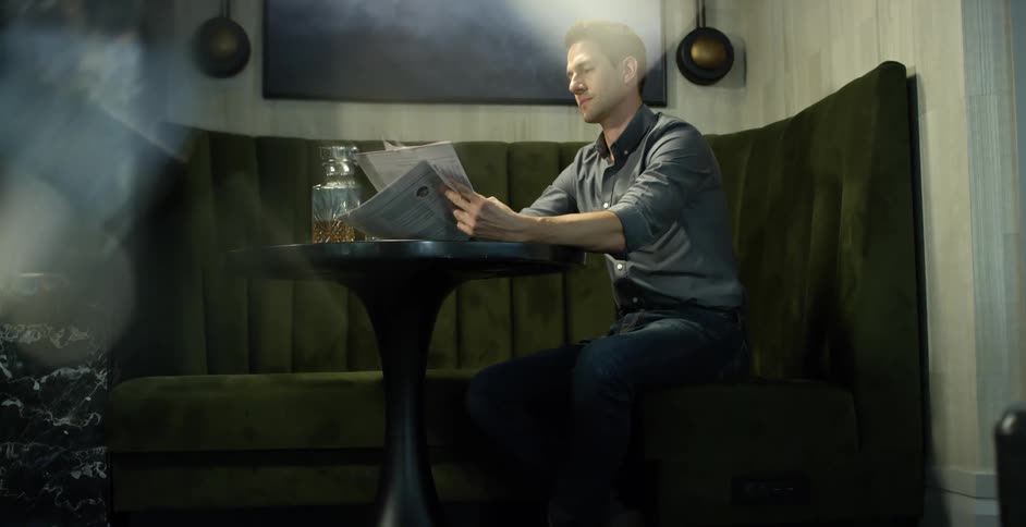 A man is sitting indoors and reading a newspaper