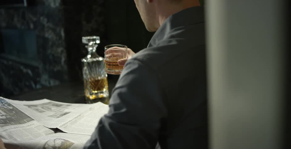 A man reads the newspaper and sips on a drink