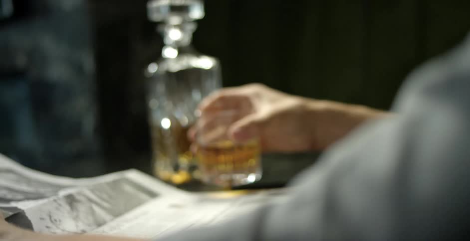 Person sits reading newspaper while having a drink