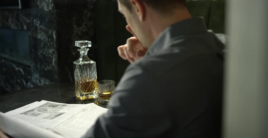 Man closes carafe and picks up drink while reading newspaper at table