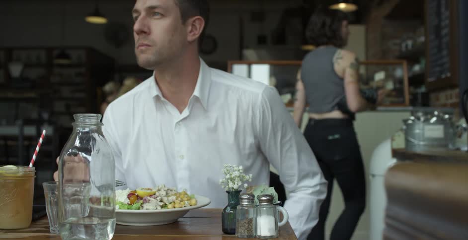 Man with a white shirt sitting at a table eats food in a cafeteria