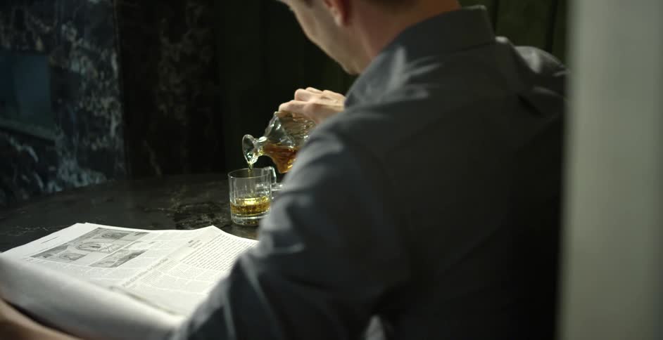 Man sitting at table in front of newspaper pours drink from carafe