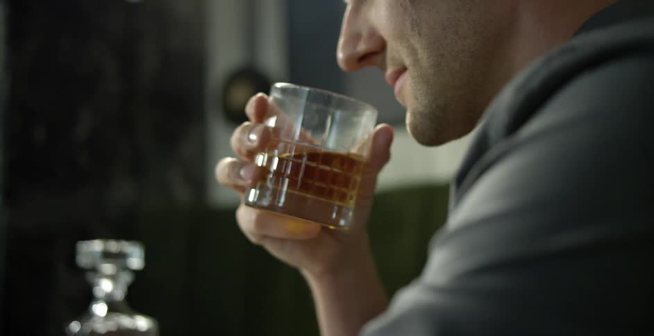 A man shakes a glass of liquor to smell it before taking a sip