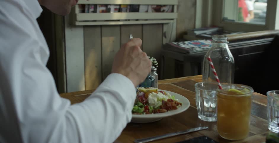 Male eats a salad alone in a restaurant as other patrons sit outside to dine