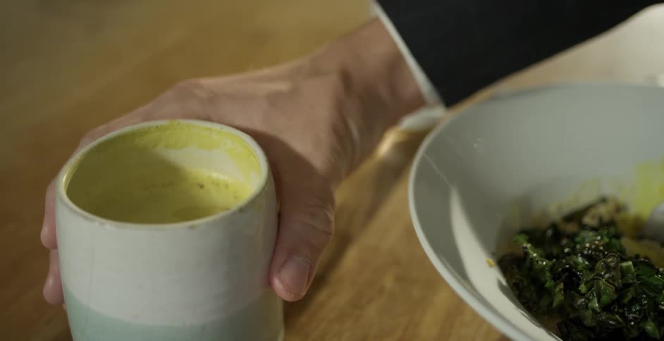 Caucasian hand grabs a cup of beverage that is sitting next to a bowl of food