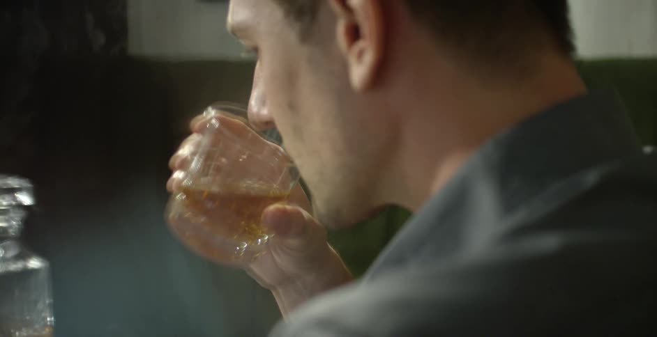 A man drinks whiskey from a short glass