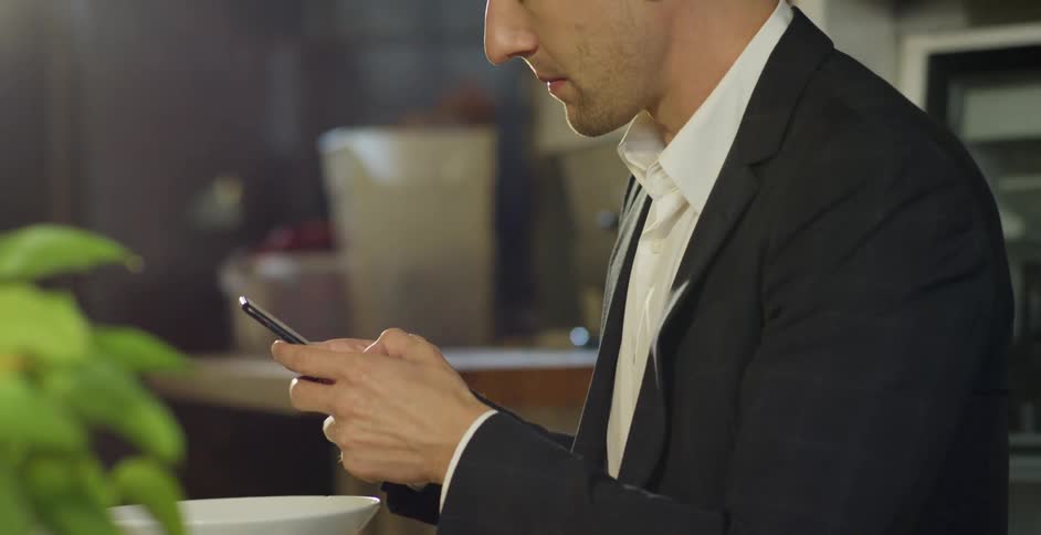 A man uses a smartphone while sitting in front of food at a dining table