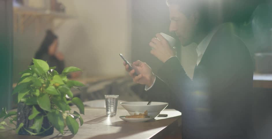 Man wearing a suit checks his phone while eating breakfast in a restaurant