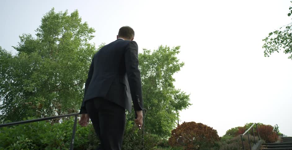 Man in business suit with smartphone in hand climbs the stairs of a park at day