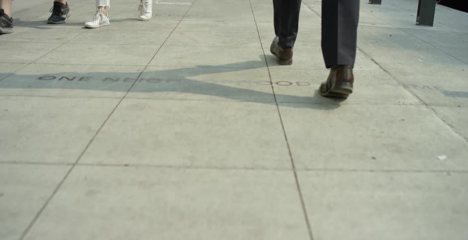 Man with a black suit and a pair of brown formal shoes walks down a street