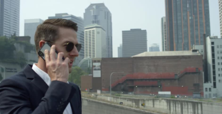 Man wearing business suit and sunglasses talk on the smartphone in front of the city skyscrapers