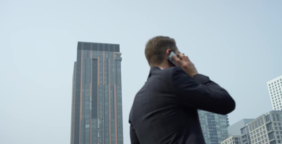 Man holds a cell phone to his ear as he walks in the city near the office buildings