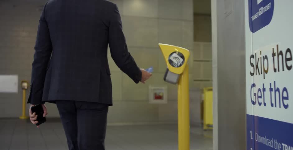 A man with a suit and a smart phone putting a card up to a sensor then walking towards an escalator
