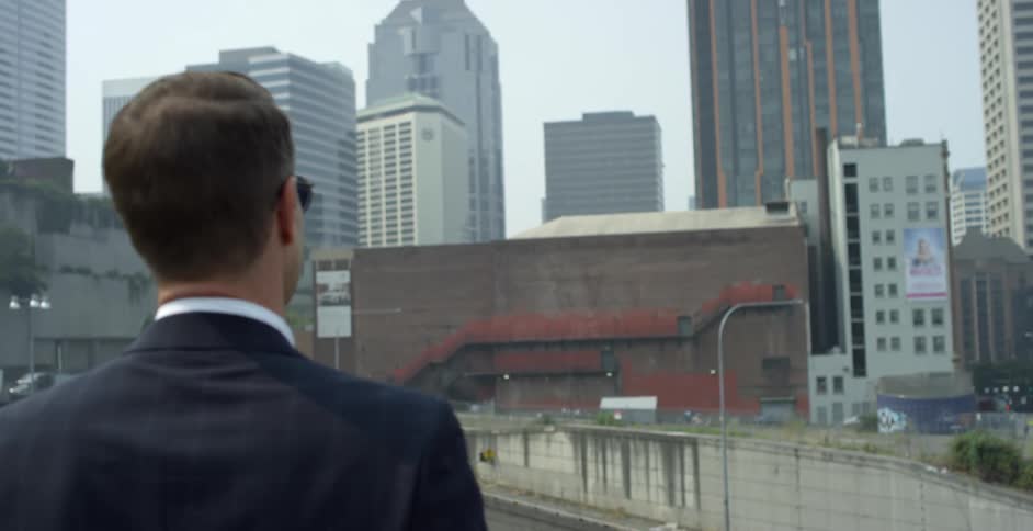 A man in a suit stands and looks towards a downtown area at office buildings