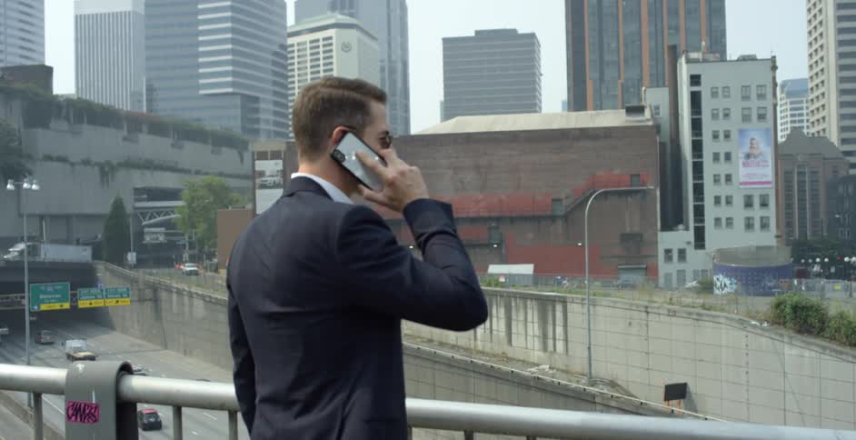 Man in a suit talks on a smartphone while looking at city downtown