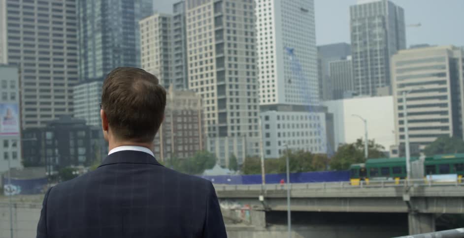 A man stands on a pedestrian balcony and looks out to the city skyline then puts his phone to his ear