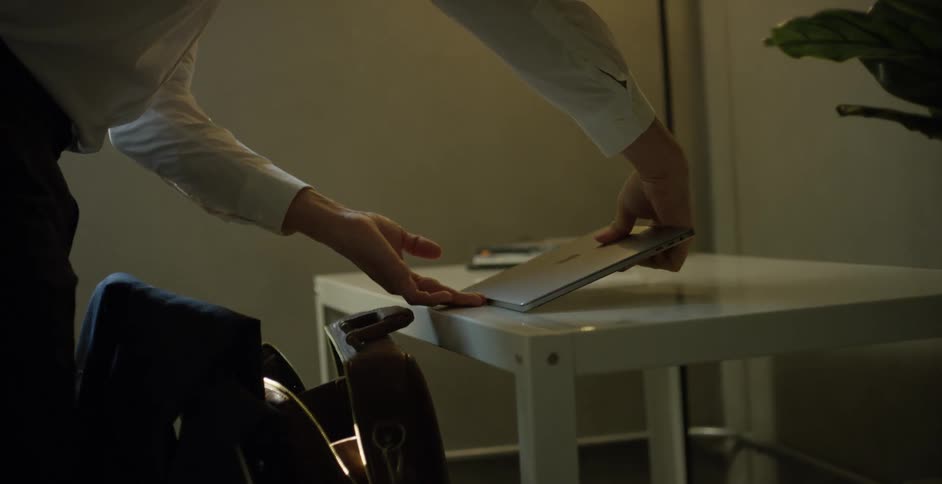 A man lifts his laptop case from the floor and places his laptop within