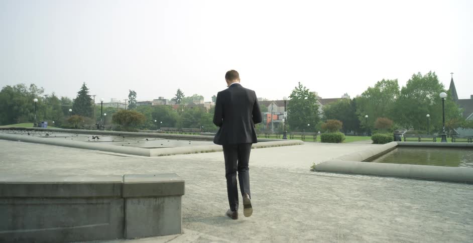 Man wearing business suit walks past man made ponds
