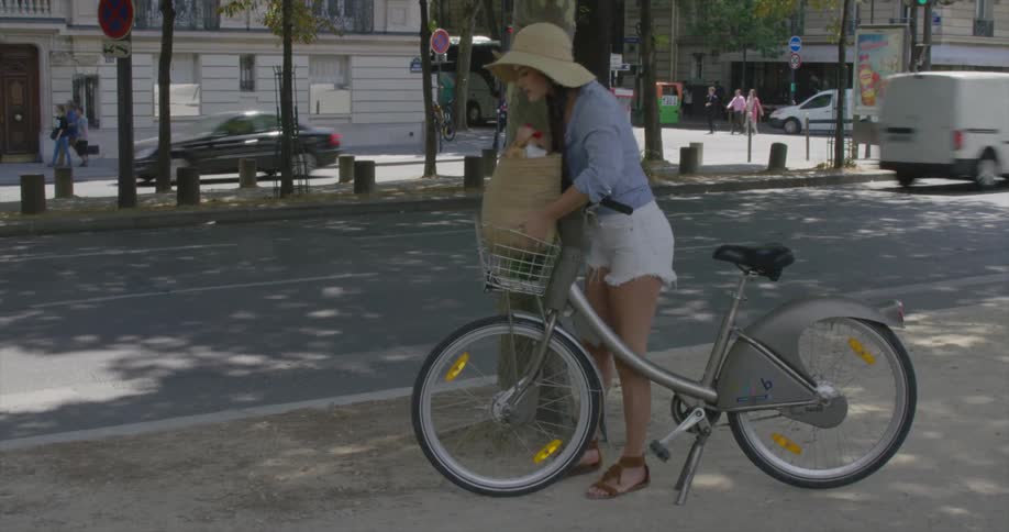 A woman placing a bag in a basket attached to her bicycle