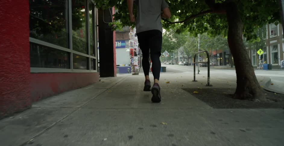 A man jogs on a city sidewalk on a summer day