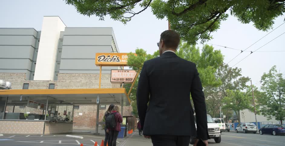 A man in a suit walks down a sidewalk in a city during the day