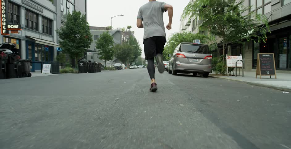 A man in athletic wear runs down a city street on a cloudy day