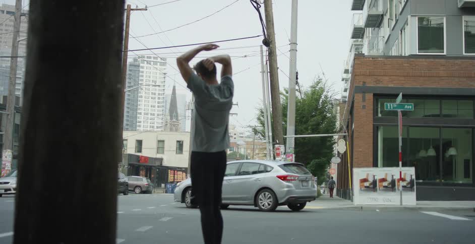 Middle aged man stands and warms up to run on the street in the city center