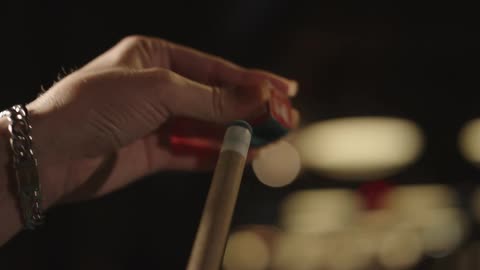 A person polishes their pool cue with chalk