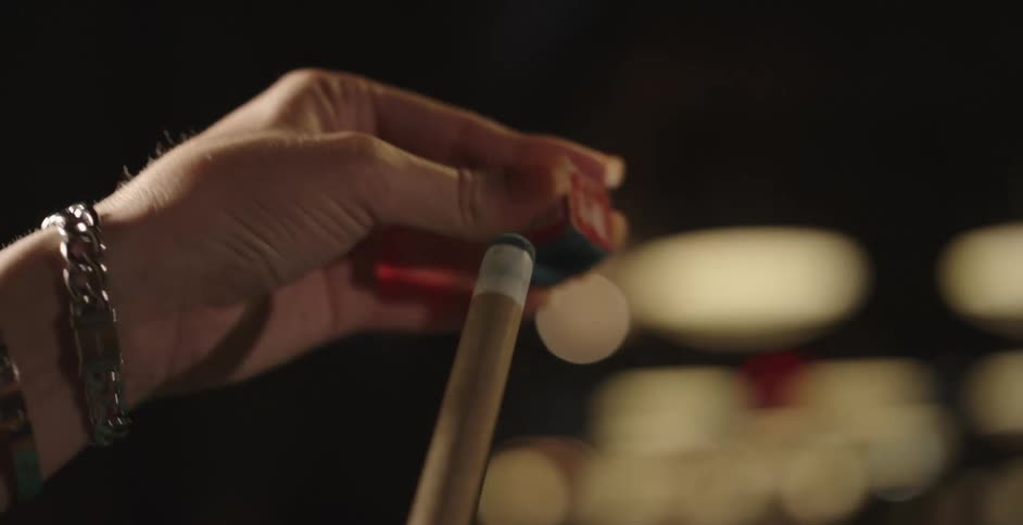 A person polishes their pool cue with chalk